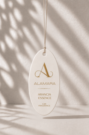 Alamara Arancia Essence car fragrance hanging against a neutral background with shadows.