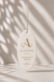 Alamara Moonlight Serene car fragrance hanging against a neutral background with shadows.
